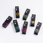 Hét fekete doboz CBD Olaj 5% Full Spectrum - 500 mg | 10 ml, mindegyik egyedi színű akcentussal - sárga, zöld, kék, lila, piros és ezüst - van elhelyezve egy laza körben, fehér felületen.