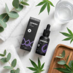 Egy üveg és egy doboz Happy Garden CBD Olaj CBN + CBD + CBG (4000 mg, 30 ml) cseppentővel, körülötte kannabiszlevelek, eukaliptusz, egy pohár víz és fehér törülközők a márványon - ideális a CBD Europe rajongói számára.