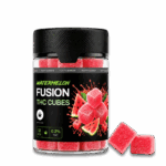 Egy „Happy H Gummies Görögdinnye – 10 mg / db – Strong Edition, 12 db” feliratú üvegben piros, cukorral bevont görögdinnye-ízű gumicukrok láthatók. Az üveg mellett két gumicukor fekszik, a címke pedig azt jelzi, hogy összesen 12 darab van benne.